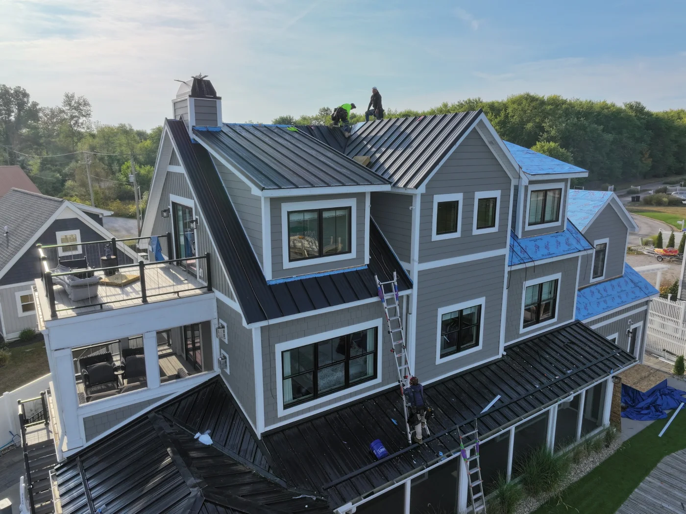 Roofers installing dark metal panels on a multistory home