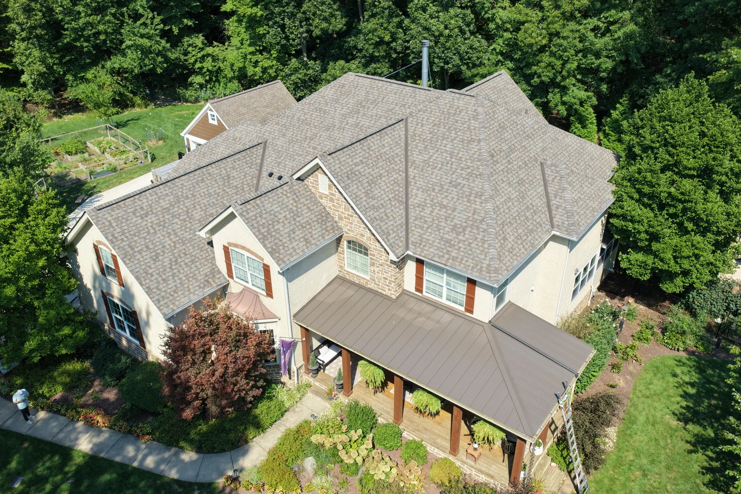 Completed shingle roof and metal porch roof on a home surrounded by trees